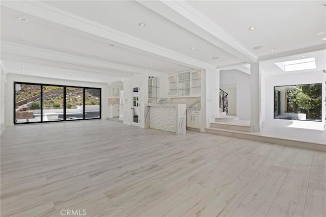 unfurnished living room with crown molding, a skylight, and light hardwood / wood-style floors