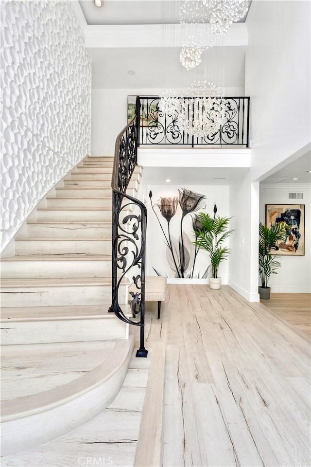 stairway with wood-type flooring, a towering ceiling, and a chandelier