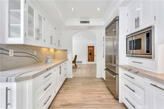 kitchen featuring white cabinetry, built in appliances, crown molding, and light hardwood / wood-style floors