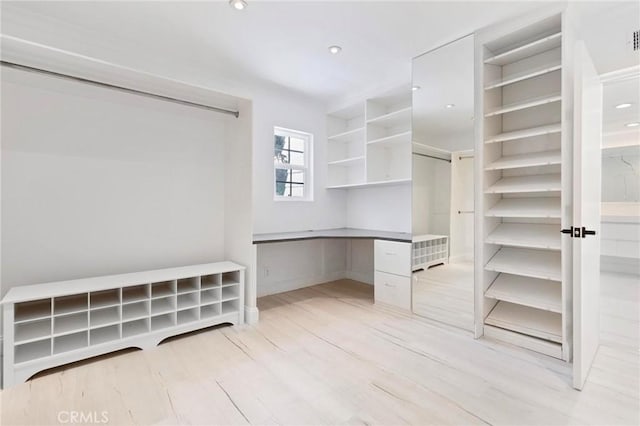 spacious closet featuring built in desk and light hardwood / wood-style flooring