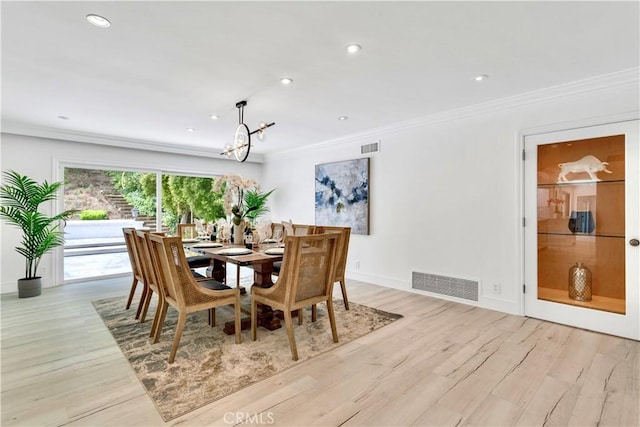 dining area featuring ornamental molding, an inviting chandelier, and light hardwood / wood-style flooring