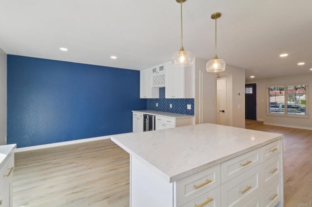 kitchen with white cabinetry, tasteful backsplash, a kitchen island, decorative light fixtures, and light wood-type flooring