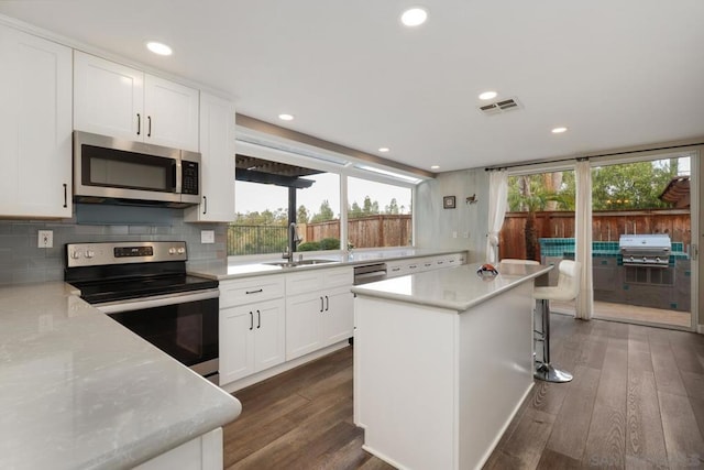 kitchen featuring white cabinetry, sink, a center island, stainless steel appliances, and light stone countertops