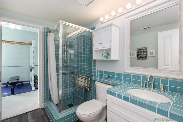 bathroom featuring tasteful backsplash, vanity, tiled shower, and toilet