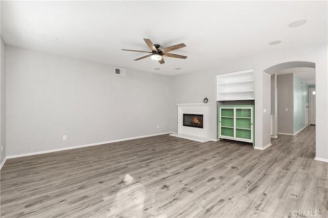 unfurnished living room with ceiling fan, built in features, and light hardwood / wood-style floors