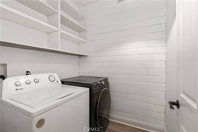 laundry room with wooden walls, dark wood-type flooring, and independent washer and dryer