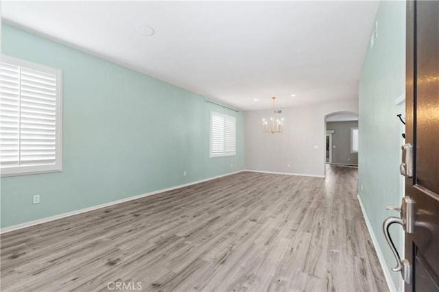 unfurnished room with a notable chandelier and light hardwood / wood-style flooring