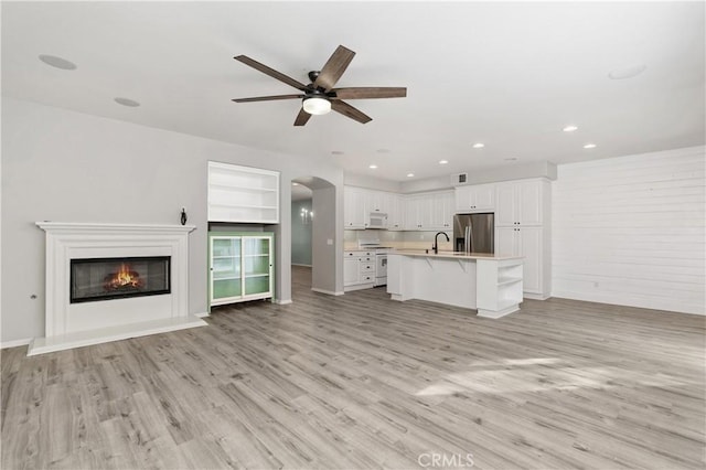 unfurnished living room with sink, built in shelves, light hardwood / wood-style floors, and ceiling fan