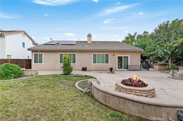 rear view of property with a fire pit, a lawn, central AC unit, a patio area, and solar panels