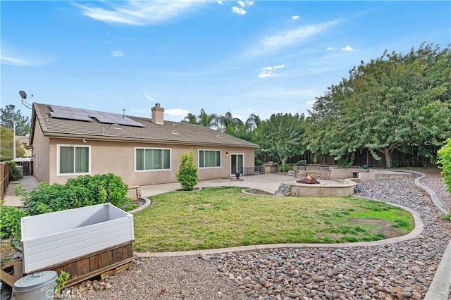 rear view of property featuring a fire pit, a lawn, a patio, and solar panels