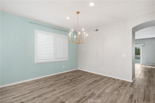 spare room with an inviting chandelier and hardwood / wood-style flooring