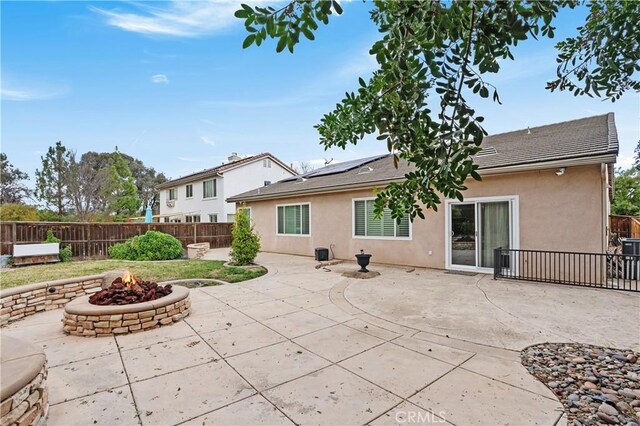 back of house with a fire pit, a patio area, and solar panels