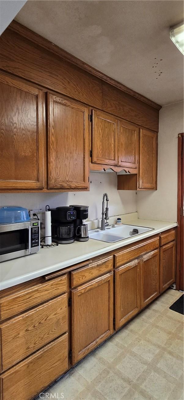 kitchen featuring light floors, stainless steel microwave, a sink, and brown cabinetry