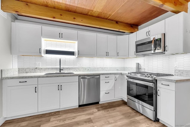 kitchen with appliances with stainless steel finishes, sink, white cabinets, beam ceiling, and light hardwood / wood-style flooring