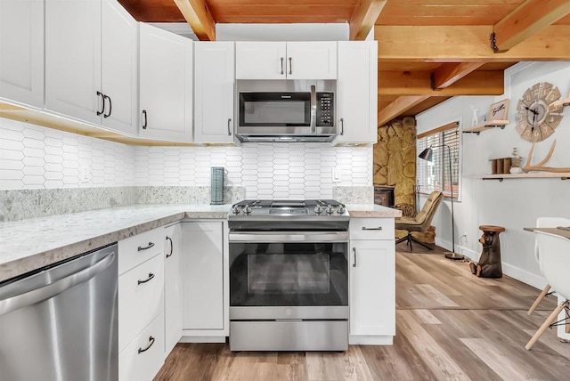 kitchen with stainless steel appliances, beam ceiling, light stone countertops, and white cabinets