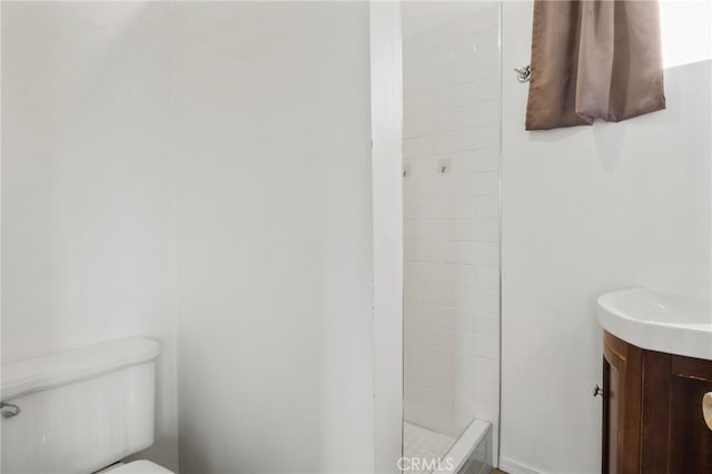 bathroom with a tile shower, vanity, and toilet