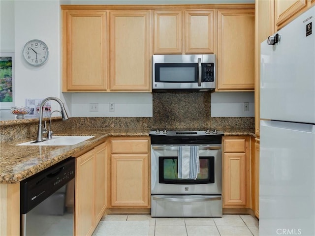 kitchen with sink, stainless steel appliances, light tile patterned flooring, light brown cabinetry, and dark stone counters