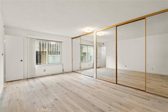 unfurnished bedroom with multiple closets, a textured ceiling, and light hardwood / wood-style floors