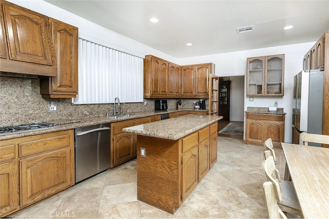 kitchen featuring sink, appliances with stainless steel finishes, a center island, light stone countertops, and decorative backsplash