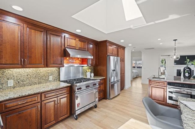 kitchen featuring appliances with stainless steel finishes, tasteful backsplash, hanging light fixtures, light stone counters, and light hardwood / wood-style flooring