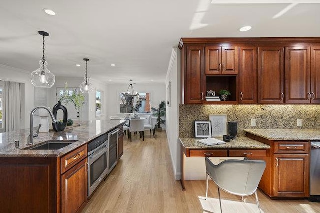 kitchen with sink, appliances with stainless steel finishes, backsplash, light stone countertops, and decorative light fixtures