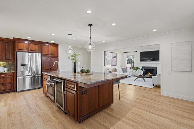 kitchen with a breakfast bar, appliances with stainless steel finishes, a kitchen island with sink, stone countertops, and decorative light fixtures