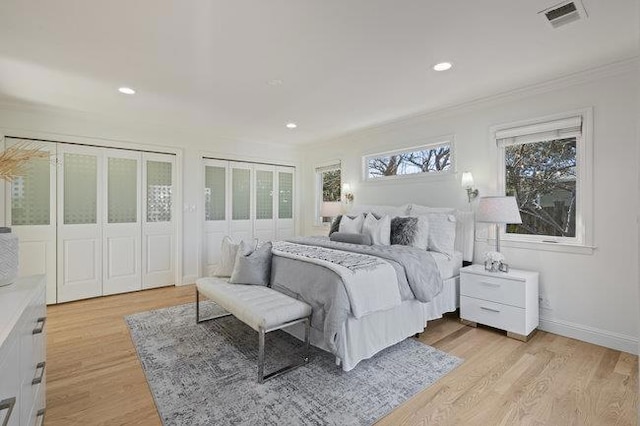 bedroom featuring multiple closets, ornamental molding, and light hardwood / wood-style floors