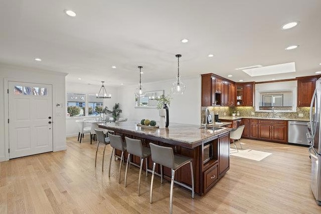 kitchen featuring pendant lighting, tasteful backsplash, stainless steel appliances, light stone countertops, and light hardwood / wood-style flooring