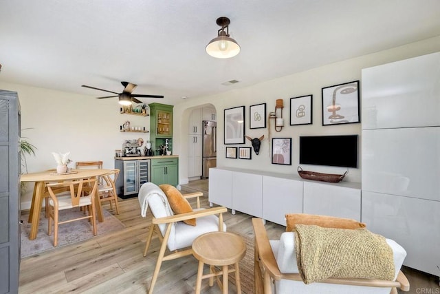 living room featuring ceiling fan, indoor bar, beverage cooler, and light wood-type flooring