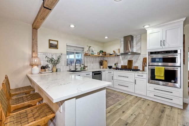 kitchen featuring a breakfast bar, white cabinetry, kitchen peninsula, stainless steel appliances, and wall chimney exhaust hood