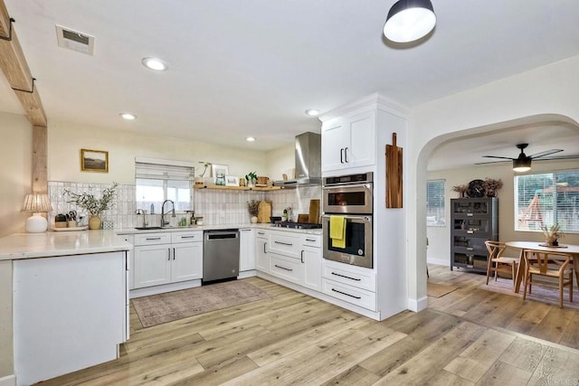 kitchen with sink, appliances with stainless steel finishes, a wealth of natural light, white cabinets, and wall chimney exhaust hood