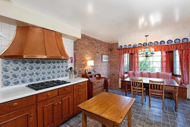 kitchen featuring premium range hood, brick wall, decorative light fixtures, a notable chandelier, and gas stovetop