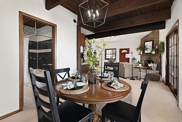 carpeted dining room featuring an inviting chandelier, a stone fireplace, wooden ceiling, and beamed ceiling