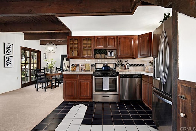 kitchen with appliances with stainless steel finishes, tasteful backsplash, beam ceiling, dark colored carpet, and an inviting chandelier