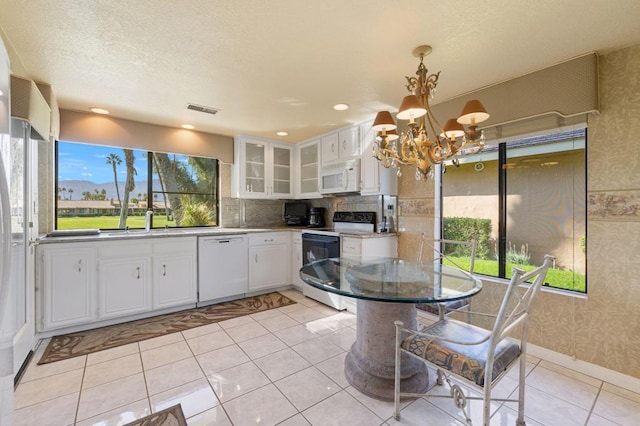 kitchen with sink, white appliances, white cabinetry, decorative light fixtures, and a chandelier