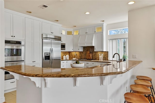 kitchen featuring premium range hood, a breakfast bar area, built in appliances, and kitchen peninsula