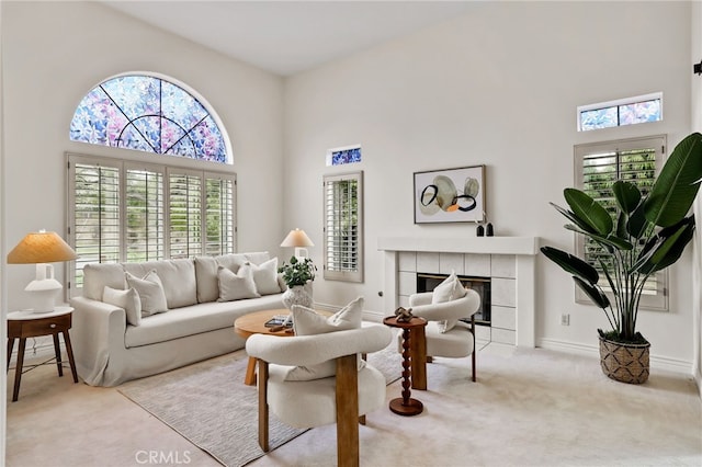 carpeted living room featuring a tile fireplace and a towering ceiling