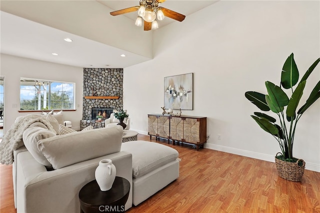 living room featuring a stone fireplace, ceiling fan, and light hardwood / wood-style flooring