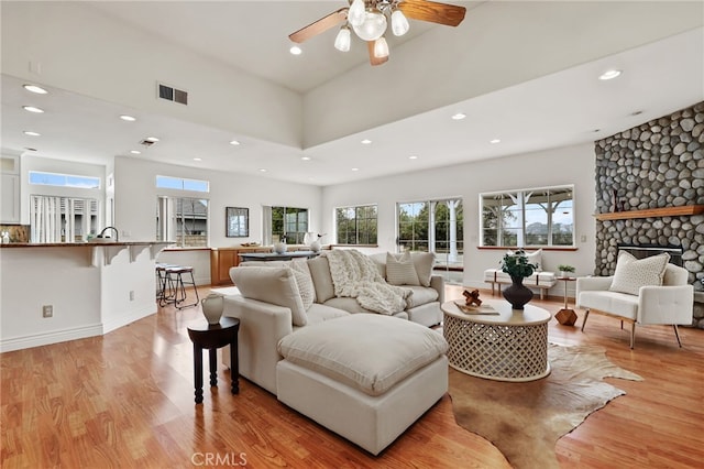 living room with ceiling fan, a stone fireplace, and light hardwood / wood-style flooring