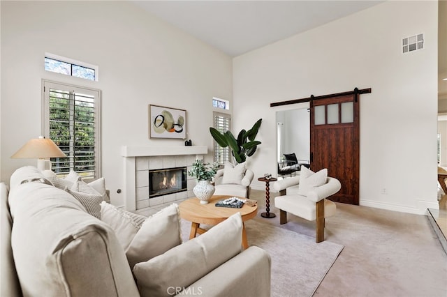 living room with a tiled fireplace, a towering ceiling, light colored carpet, and a barn door