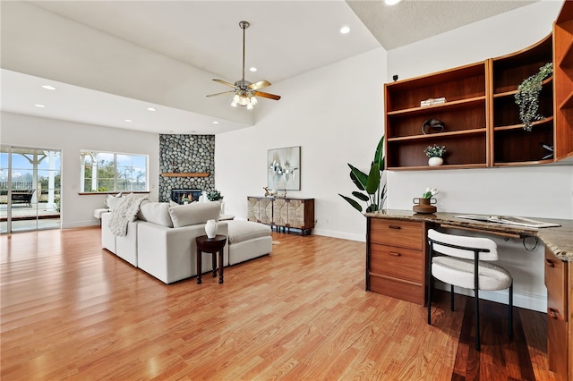 home office featuring ceiling fan, a stone fireplace, built in desk, and light wood-type flooring