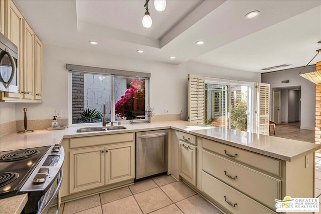 kitchen with kitchen peninsula, sink, a tray ceiling, stainless steel appliances, and cream cabinets