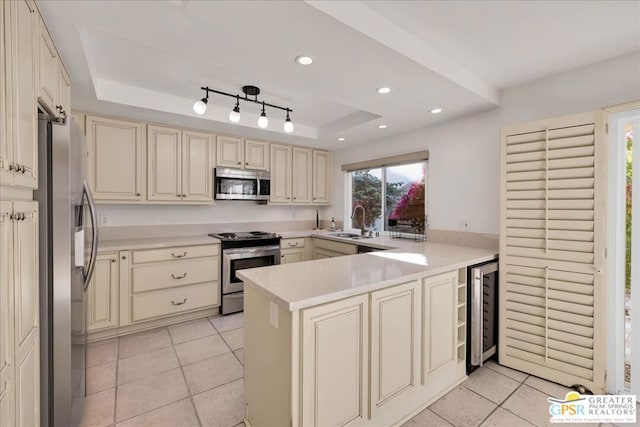 kitchen with sink, a tray ceiling, kitchen peninsula, stainless steel appliances, and beverage cooler