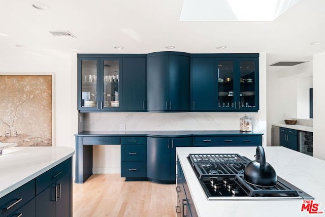 kitchen featuring blue cabinets, light stone counters, light wood-type flooring, black gas stovetop, and decorative backsplash