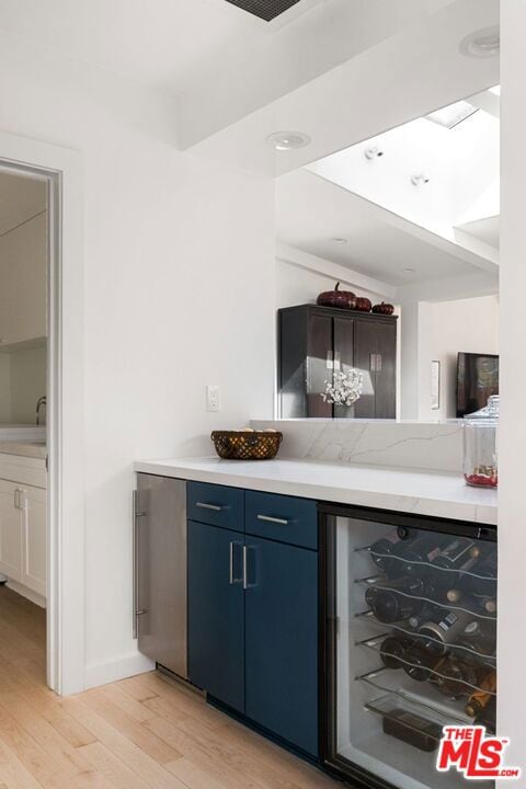 bar featuring blue cabinetry, wine cooler, refrigerator, and light hardwood / wood-style flooring