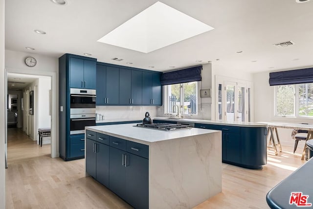 kitchen with a kitchen island, a skylight, sink, stainless steel appliances, and blue cabinetry