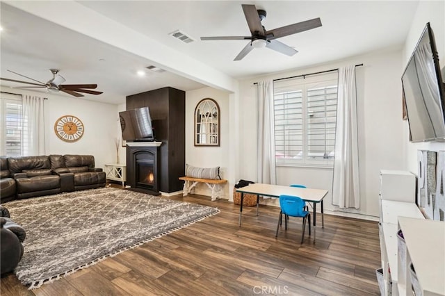 living area featuring a lit fireplace, dark wood-type flooring, visible vents, and a ceiling fan