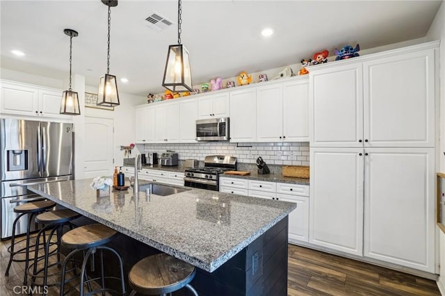 kitchen featuring a center island with sink, appliances with stainless steel finishes, white cabinets, a sink, and dark stone countertops