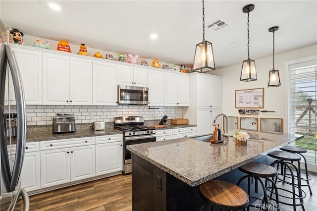 kitchen with stainless steel appliances, white cabinetry, a sink, and a center island with sink