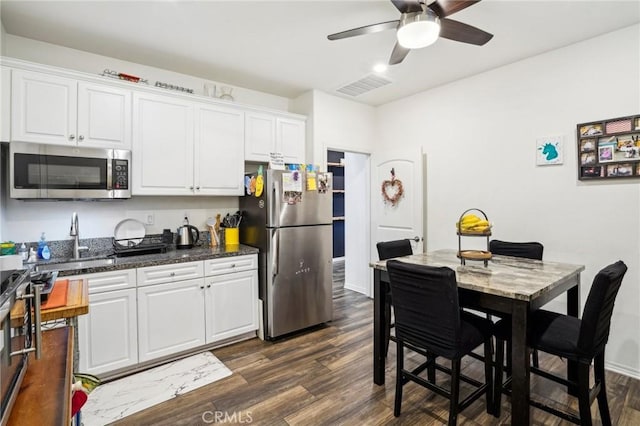 kitchen with dark wood finished floors, stainless steel appliances, visible vents, white cabinets, and a sink